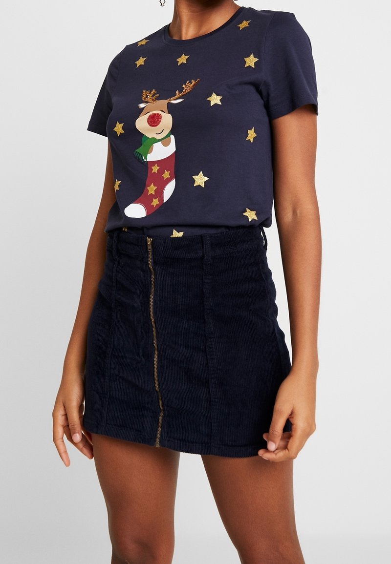 Marinblå bomullströja med en ren-klippning och gyllene stjärnor; ihop med en mörk kordflamskjol med blixtlås fram och strukturerad yta.