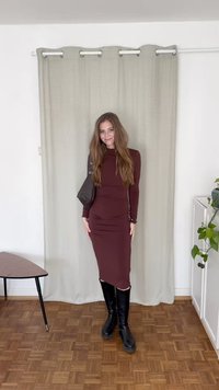Vestido de manga longa, cor bordô, com uma silhueta ajustada e franzido lateral. Combinado com botas pretas até aos joelhos e uma pequena mala de ombro.