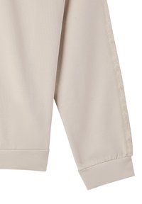Manica di felpa color beige chiaro con una texture liscia, polsini a costine e un nastro decorativo lungo il lato che presenta un motivo sottile.