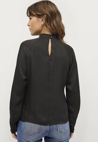 Zwarte blouse met lange mouwen en een hoge halslijn, met een keyhole aan de achterkant en knopen. Glad textuur en een comfortabele pasvorm, gecombineerd met denim.