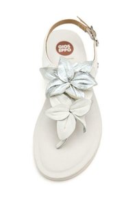 Sandelia blanca con dos adornos en forma de flor, uno de cuero plateado y otro de un material suave blanco, asegurada con una correa ajustable en el tobillo.
