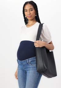 Svart toteveske med strukturert form og glatt lærtekstur, kombinert med en ribbestrikket kremtop og blå denimjeans, båret over et marineblått stretchbelte.