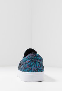 Teniska s vrchní částí z tkaniny se vzorem v modrých, černých a růžových odstínech. Má bílou gumovou podrážku a kulatou špičku.