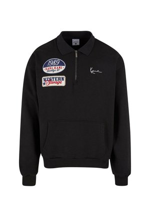 Sort pullover trøje med lynlås-krave, der har tre broderede patches: "1989", "KARL KANI" og "WESTERN Savage." Foran er der en kengurulomme.