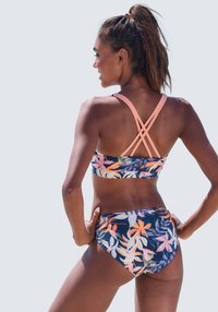 Kvetinový bikiny set s námorní základňou, tropickými listovými potlačami v oranžovej a ružovej farbe a prekríženými ramienkami s broskyňovými detailami.