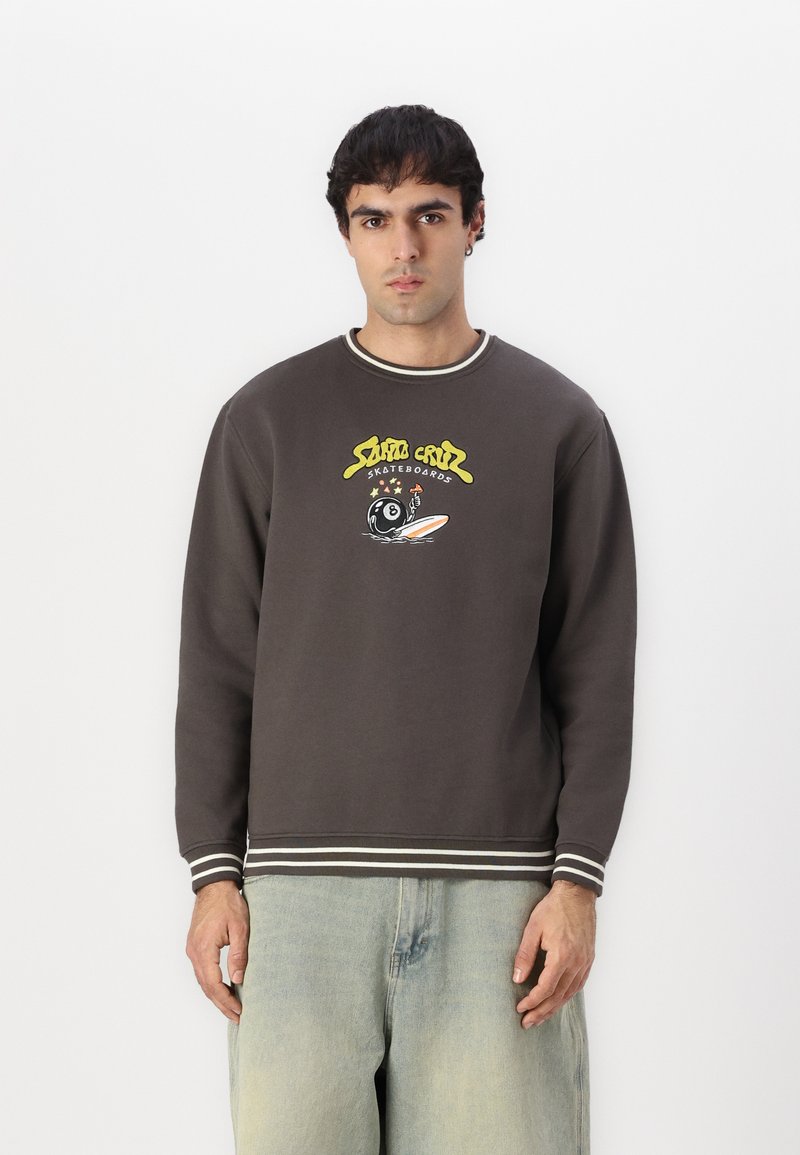Felpa marrone con polsini e scollatura a coste bianchi e grigi. Presenta un design grafico colorato con testo e una tavola da surf.