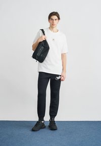 Biele tričko s krátkym rukávom s logom, čierne tepláky s bielym logom, čierne tenisky a čierna crossbody taška. Jednoduchý, funkčný dizajn.