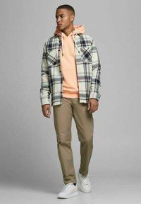 Karierter Flanellhemd in Creme und Marineblau über einem orangenen Hoodie, kombiniert mit beigefarbenen Hose und weißen Sneakern. Einfaches, legeres Design.