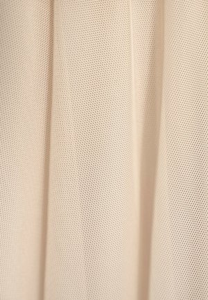 Beżowa tkanina siatkowa z drobną, perforowaną fakturą i równomiernie rozmieszczonymi okrągłymi otworami, układająca się w miękkie fałdy.