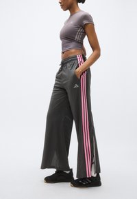 A szürke sportnadrág rózsaszín oldalsávokkal és gombos sliccekkel rendelkezik. A hozzáillő szürke crop top finom márkajellel és testhez simuló szabással készült.