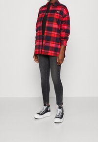 Camicia in flanella a quadri rossi e blu, con chiusura a bottoni, abbinata a jeans scuri aderenti e sneakers nere alte. Design minimalista, stile versatile.