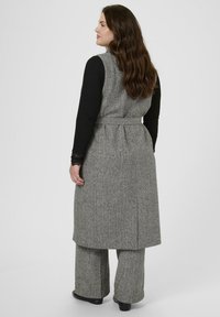 Harmaa tweed-pitkä liivi vyöllä, jossa on korkea halkio ja takataskut, yhdistettynä samanvärisiin leveälahkeisiin housuihin. Rakenteellinen kangas.