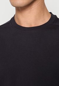 Zwarte crewneck-trui, gemaakt van zacht stof, met een gladde textuur en een eenvoudig ontwerp. Close-up opname die de details van de halslijn benadrukt.