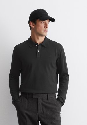 Black long-sleeve polo shirt with a buttoned collar, paired with dark gray tailored pants. The individual wears a matching black cap.