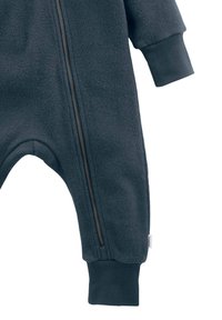 Donkerblauwe fleece jumpsuit met lange mouwen, een rits aan de voorkant en ribgebreide manchetten. Heeft een gladde textuur en gebogen beenopeningen aan de onderkant.
