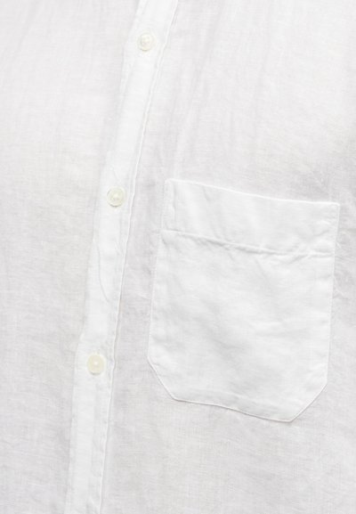 Λευκό λινό πουκάμισο μπροστά με τρία ορατά κουμπιά και τσέπη στο στήθος στη δεξιά πλευρά.