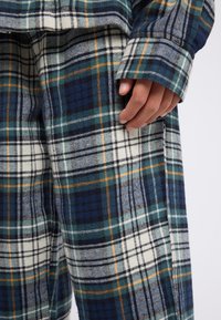 Primer plano de una mano descansando sobre una tela a rayas azul, verde, blanca y naranja de una camisa de manga larga y pantalones a juego.