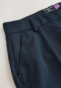 Tumši jūras zila bikses, izgatavotas no gludas auduma, ar plakanu jostasvietu, sānu kabatām un kārtīgu izgriezumu dizainu. Redzama birka ar zīmola nosaukumu.