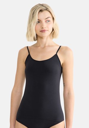 Blonde woman wearing a black fitted camisole with thin straps, looking slightly to her left on a plain light background.