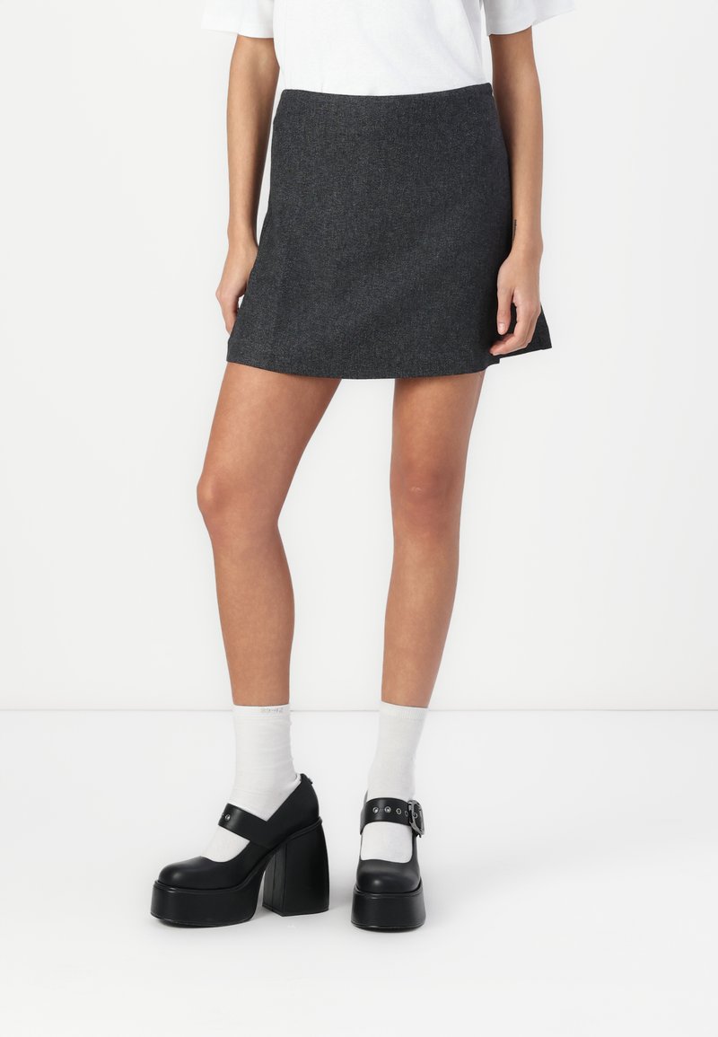 Gray, textured mini skirt with a slight flare, paired with black platform shoes featuring a strap and buckle, worn over white socks.