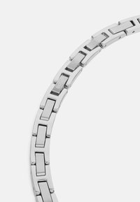 Silberner Metallarmreifen mit rechteckigen Gliedern, polierter Oberfläche und graviertem Logo. Sanfte Textur und modernes Design.