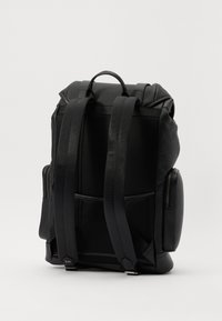 Rucsac negru cu material texturat, curele căptușite și un mâner de sus. Buzunare laterale cu fermoar. Design elegant și modern.