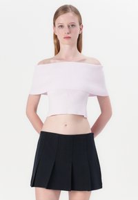 Lichtroze off-shoulder ribbelcrop top gecombineerd met een zwarte geplooide minirok. De top heeft een aansluitend ontwerp, terwijl de rok gestructureerde plooien heeft.