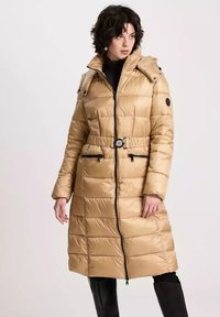 Beżowy kurtka ocieplana z zamkiem błyskawicznym z przodu, z paskiem w talii, dużym kołnierzem, kieszeniami bocznymi i czarnymi akcentami z metalu, z pudełkowym pikowanym wzorem.