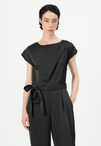 Top de satén negro con escote redondo, mangas cortas y un detalle de lazo lateral en la cintura. Textura suave, diseño minimalista.