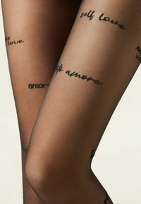 Schwarze transparente Strümpfe mit aufgedrucktem Text in verschiedenen Schriftarten, darunter Phrasen wie "self love" und "amore" über die Beine verteilt.