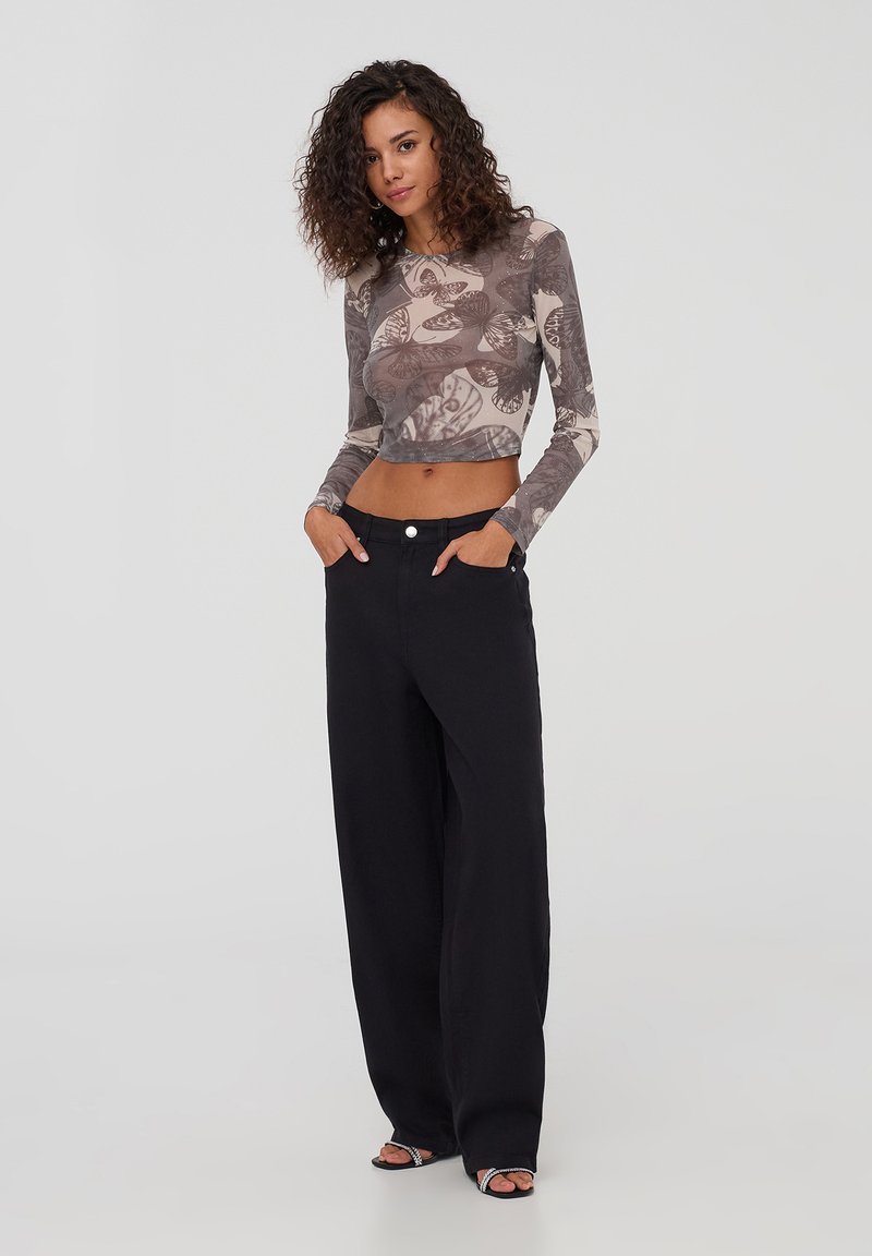 Crop top a maniche lunghe con motivo a farfalla in tonalità di grigio e beige, abbinato a pantaloni neri a vita alta e a gamba larga.