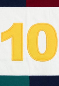 Tkanina haftowana z numerem "10" w kolorze żółtym, na białym tle, z kolorowymi sekcjami w zielonym, granatowym i burgundowym.