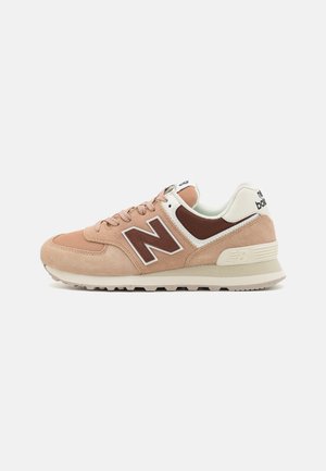 Sneakers en cuir suédé tan avec un logo en cuir marron, des accents blancs et une semelle en caoutchouc texturée. Le design comprend un laçage et un col rembourré.