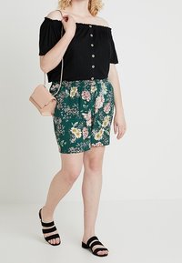 Svart axelbandslös topp med knappar, blommönstrade gröna shorts och svarta sandaler. Inkluderar en liten rosa crossover-väska.