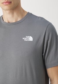 Harmaa lyhythihainen t-paita pehmeästä kankaasta, jossa on valkoinen logo "The North Face" vasemmassa rintataskussa, klassinen pyöreä pääntie.