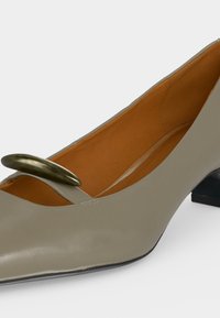Chaussure femme en cuir gris à petit talon avec une boucle ovale en bronze sur la bride et une doublure intérieure beige.