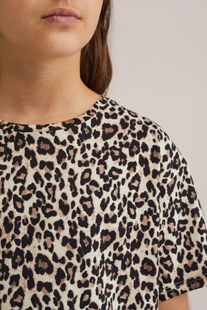 Majica s uzorkom leoparda koja ima okrugli izrez, mekani materijal i svijetlu pozadinu s tamnim točkama i teksturiranim detaljima.