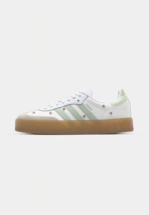 White sneaker with green accents, three stripes, floral embroidery, and a gum sole. Features a rounded toe and lace-up design.