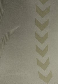 Rakea kangas muted oliivinvihreänä, jossa on vinoraitakuviot ja hienovarainen raidoitus, luoden kerroksellista visuaalista vaikutelmaa.