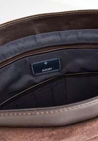 Interno della borsa in pelle marrone con rivestimento in tessuto blu navy, scomparto con zip e una piccola etichetta JOOP!. Presenta slot per l'organizzazione.