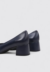 Chaussures à talon block en cuir bleu marine avec une finition lisse, bout arrondi et petit talon épais, présentant un design minimaliste et sans matériel visible.