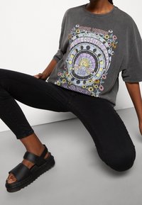 Camiseta de gran tamaño de grafito con diseño gráfico floral y texto; combinada con jeans skinny negros y sandalias de plataforma negras.