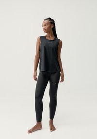 Czarny top bez rękawów z logo na klatce piersiowej, zestawiony z czarnymi, dopasowanymi legginsami z małymi wycięciami. Gładki, elastyczny materiał.