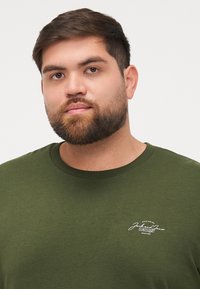 Donkergroene T-shirt van glad katoen met een ronde halslijn en een klein wit logo op de linkerborst.