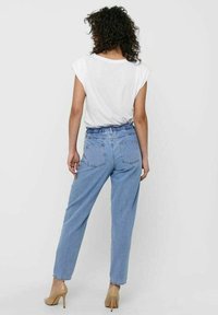 Light blue denim jeans with a relaxed fit, elastic waistband, and two back pockets. Paired with a white short-sleeve top and beige heels.