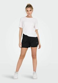 White short-sleeve t-shirt paired with black athletic shorts, featuring an elastic waistband and side pockets, worn with white sneakers.