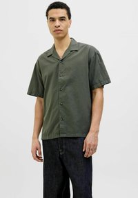 Chemise à manches courtes, couleur olive, fabriquée en tissu texturé avec un devant boutonné, présentant des boutons foncés et un col évasé.