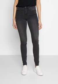 Jeans de denim negro ajustados con una cintura alta, que cuentan con bolsillos frontales y un ligero desteñido. Combinados con zapatillas deportivas blancas.