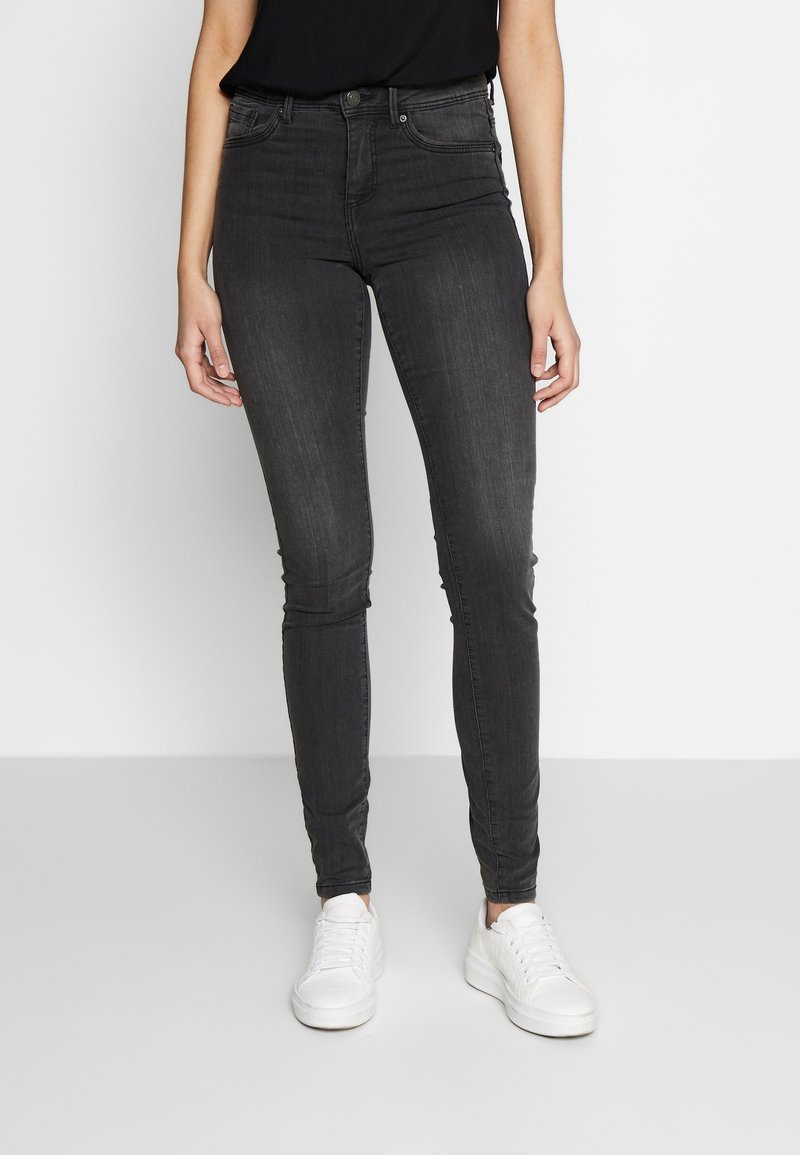 Jeans de denim negro ajustados con una cintura alta, que cuentan con bolsillos frontales y un ligero desteñido. Combinados con zapatillas deportivas blancas.