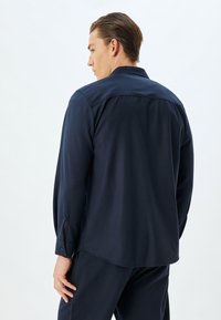 Marineblauwe overhemd met lange mouwen en een kraag, voorzien van een gladde textuur, knoopmanchetten en een lichte plooi aan de achterkant voor extra comfort.
